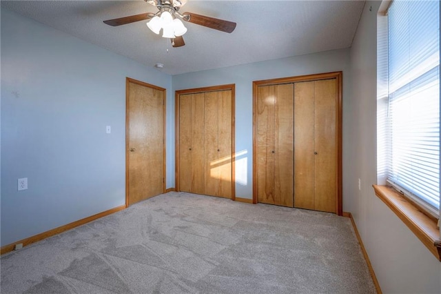 unfurnished bedroom with light carpet, ceiling fan, and multiple closets