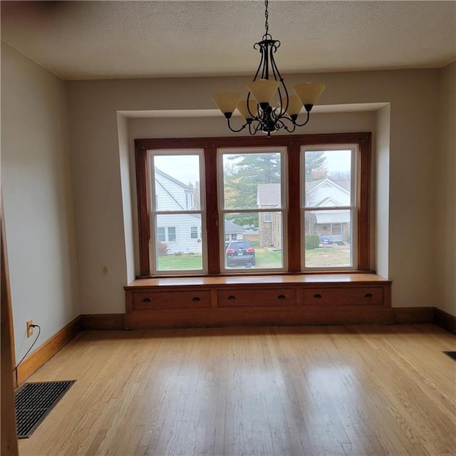 unfurnished dining area featuring light hardwood / wood-style floors, a textured ceiling, and a notable chandelier