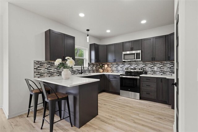 kitchen with a peninsula, a kitchen breakfast bar, backsplash, light wood-style floors, and appliances with stainless steel finishes