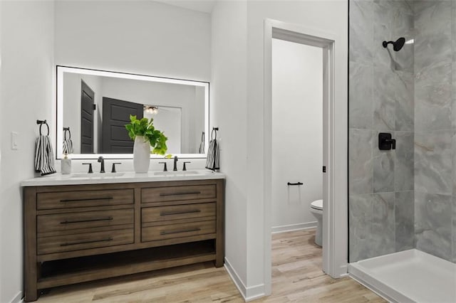 full bathroom with double vanity, wood finished floors, a stall shower, and a sink