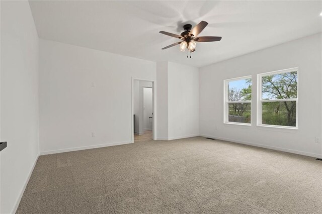 unfurnished room featuring baseboards, visible vents, a ceiling fan, and light colored carpet