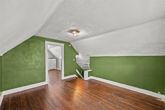 additional living space with hardwood / wood-style flooring, lofted ceiling, and a textured ceiling