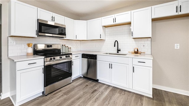 kitchen with stainless steel appliances, white cabinetry, sink, and light wood-type flooring