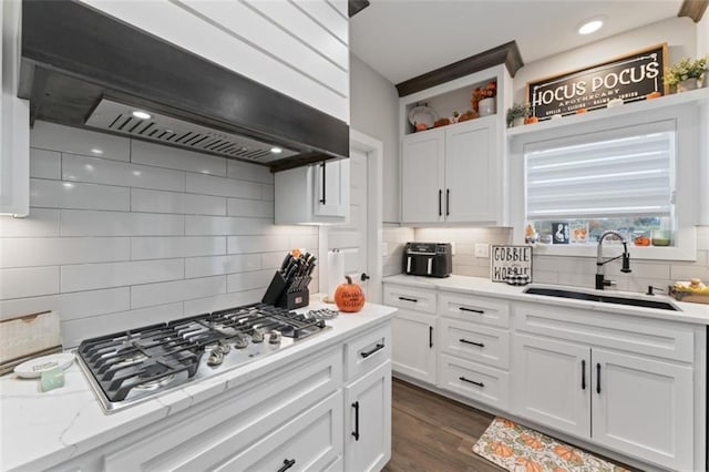 kitchen with stainless steel gas stovetop, backsplash, sink, custom range hood, and white cabinetry