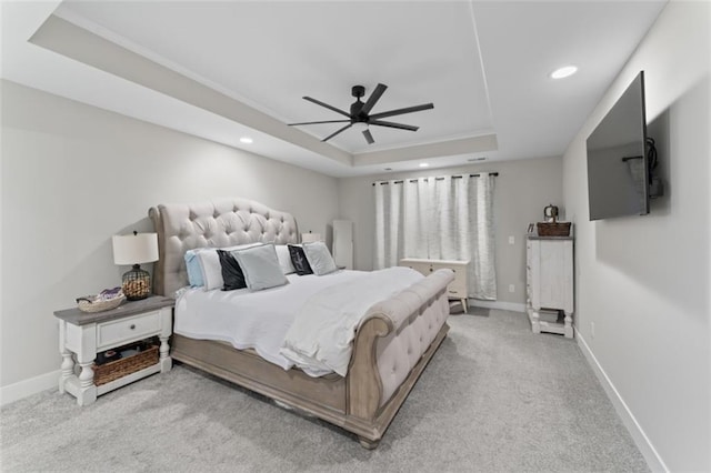 bedroom with ceiling fan, light colored carpet, and a tray ceiling