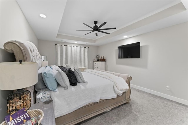 carpeted bedroom with a raised ceiling and ceiling fan