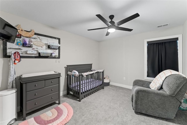 carpeted bedroom with ceiling fan and a nursery area