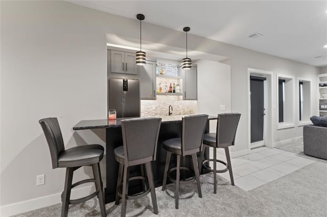 kitchen with light carpet, dark stone counters, gray cabinets, decorative light fixtures, and stainless steel refrigerator