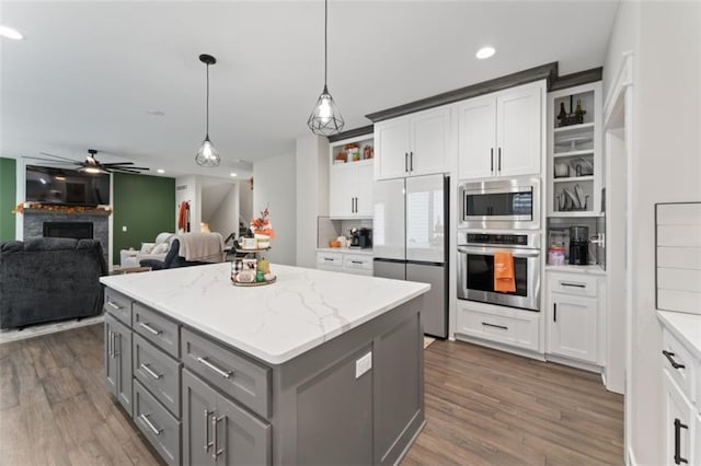 kitchen with hanging light fixtures, light stone countertops, a kitchen island, white cabinetry, and stainless steel appliances