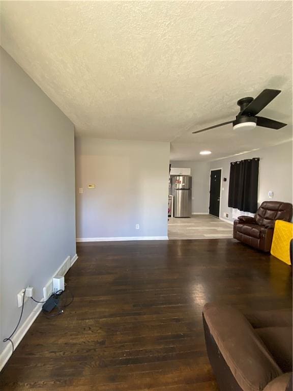 living room featuring ceiling fan, dark wood-type flooring, and a textured ceiling