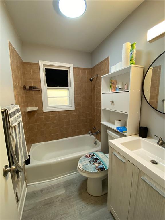 full bathroom featuring vanity, tiled shower / bath, wood-type flooring, and toilet