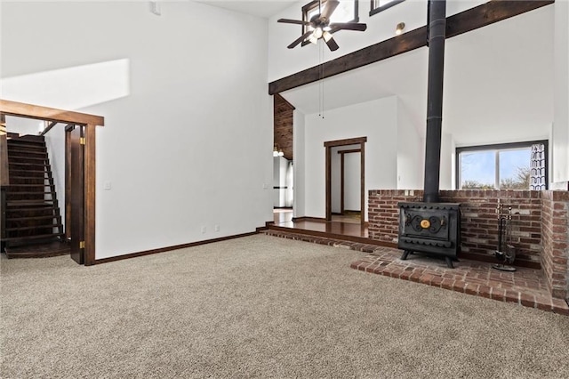 unfurnished living room featuring a wood stove, ceiling fan, carpet, and a high ceiling