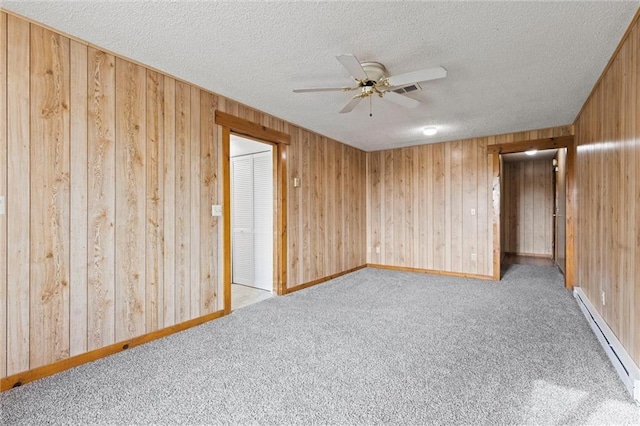 spare room featuring ceiling fan, a baseboard radiator, wood walls, a textured ceiling, and light carpet