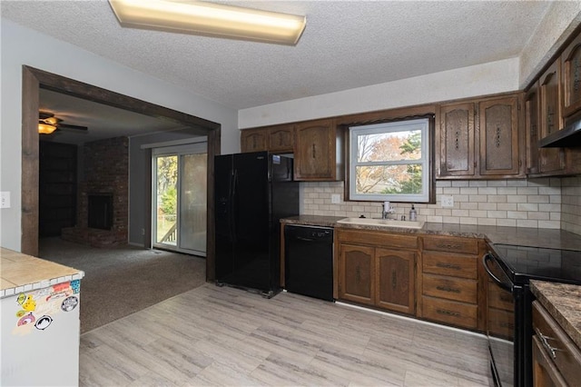 kitchen featuring sink, light hardwood / wood-style floors, decorative backsplash, a fireplace, and black appliances