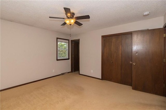 unfurnished bedroom with ceiling fan, a closet, light colored carpet, and a textured ceiling