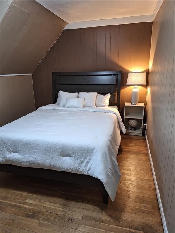 bedroom with wood-type flooring, wooden walls, and vaulted ceiling