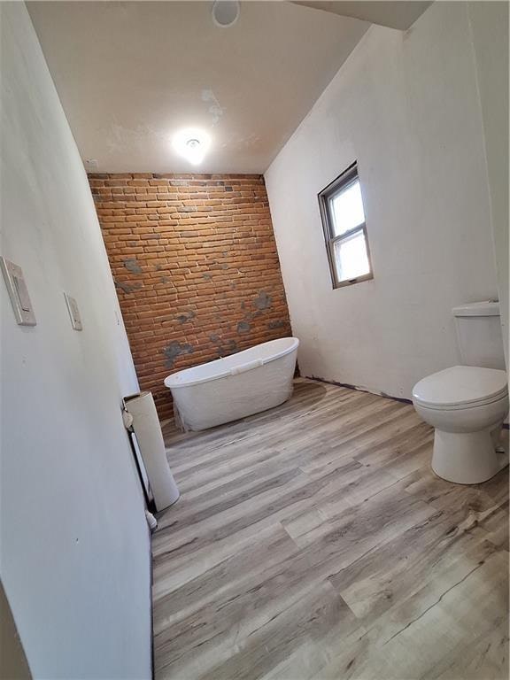 bathroom featuring a bath, hardwood / wood-style flooring, toilet, and brick wall