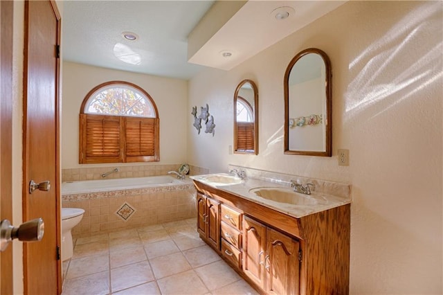 bathroom featuring a relaxing tiled tub, vanity, toilet, and tile patterned flooring