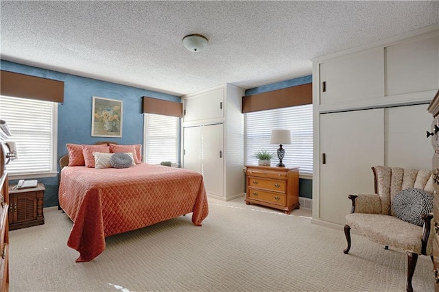 bedroom featuring multiple closets, light colored carpet, and a textured ceiling