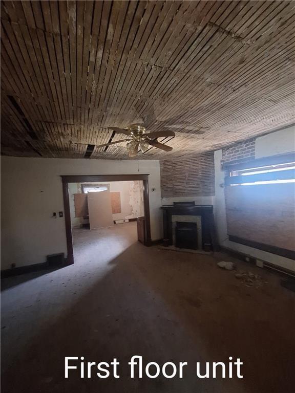 unfurnished living room with a wood stove, ceiling fan, and concrete flooring