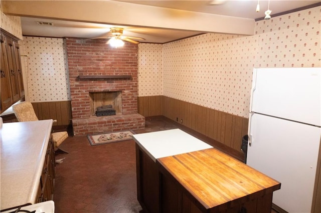 207 N Elm St, Coffeyville, KS 67337 - unfurnished living room featuring a ceiling fan, a wainscoted wall, wallpapered walls, wooden walls, and a brick fireplace