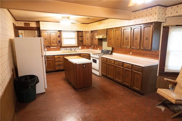 kitchen with a wealth of natural light, a center island, wall chimney exhaust hood, and white appliances