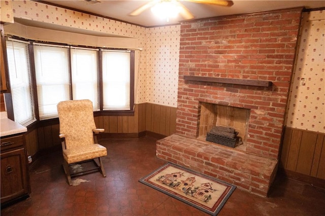 207 N Elm St, Coffeyville, KS 67337 - sitting room featuring a wainscoted wall, a ceiling fan, wood walls, wallpapered walls, and a brick fireplace