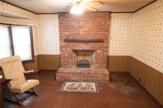 living room with ceiling fan, wood walls, ornamental molding, and a fireplace