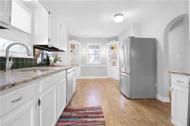 kitchen with sink, white cabinetry, light stone counters, light hardwood / wood-style flooring, and appliances with stainless steel finishes