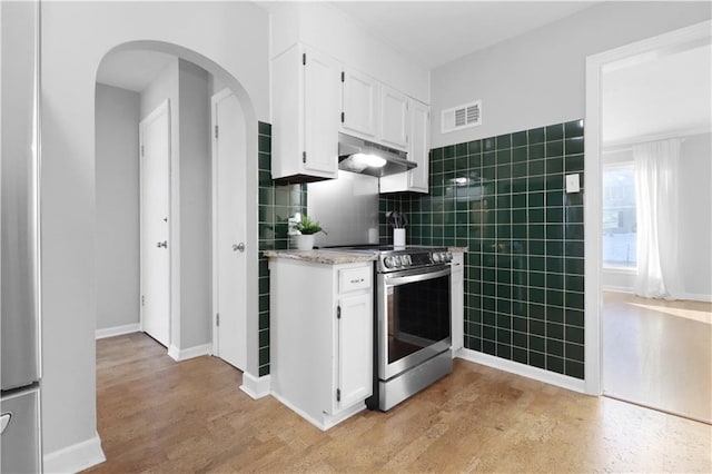 kitchen with tile walls, white cabinets, stainless steel electric stove, and light wood-type flooring