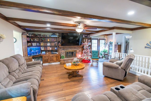 living room featuring light wood-type flooring, a brick fireplace, ornate columns, ceiling fan, and beam ceiling