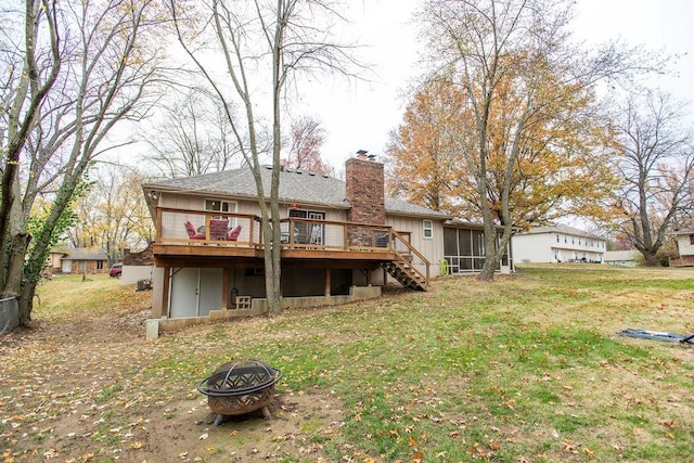 back of house with a fire pit, a sunroom, a deck, and a lawn