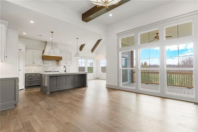 kitchen featuring custom exhaust hood, light countertops, backsplash, wood finished floors, and beamed ceiling