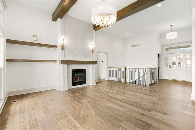 unfurnished living room featuring a chandelier, visible vents, beamed ceiling, and light wood-style flooring