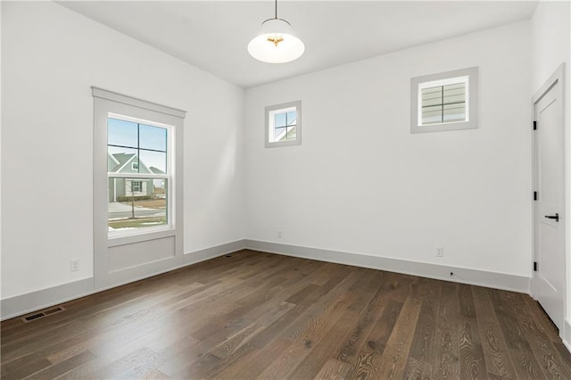 empty room with dark wood-style flooring, visible vents, and baseboards