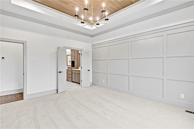 unfurnished bedroom featuring light colored carpet, ensuite bath, a tray ceiling, and wooden ceiling