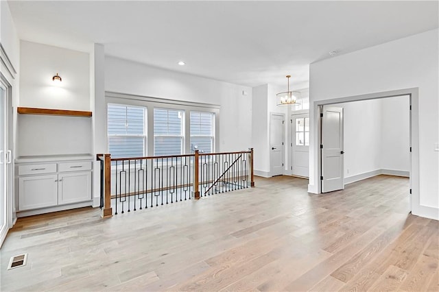 empty room with light wood-type flooring and a notable chandelier