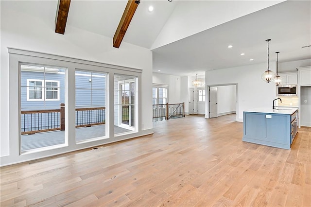 kitchen with stainless steel microwave, a kitchen island with sink, lofted ceiling with beams, light hardwood / wood-style flooring, and white cabinetry