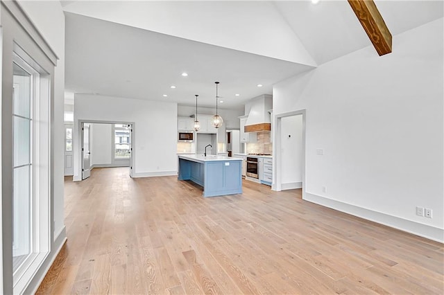 kitchen featuring pendant lighting, custom exhaust hood, a kitchen island with sink, a kitchen breakfast bar, and light wood-type flooring