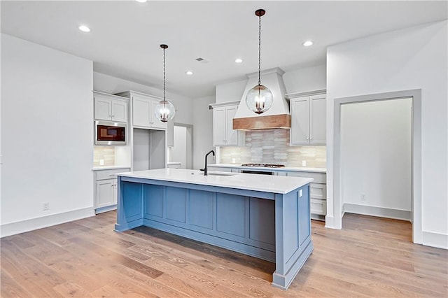 kitchen featuring sink, hanging light fixtures, light hardwood / wood-style floors, a kitchen island with sink, and custom exhaust hood