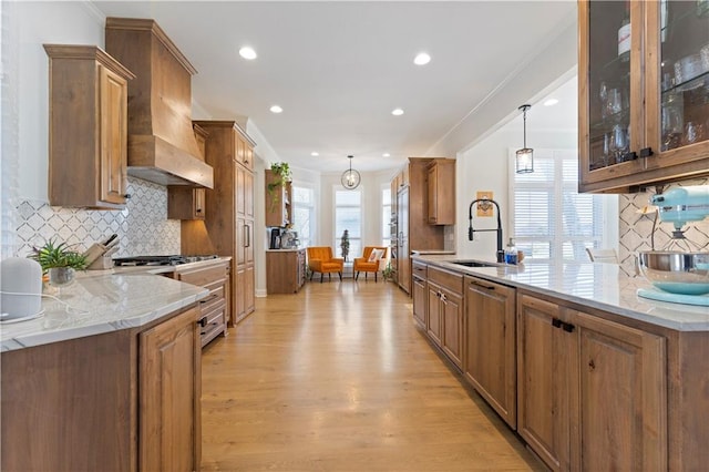 kitchen with custom exhaust hood, sink, hanging light fixtures, decorative backsplash, and light wood-type flooring