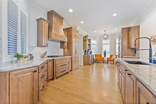 kitchen featuring pendant lighting, premium range hood, crown molding, sink, and light hardwood / wood-style floors