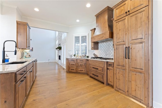 kitchen with stainless steel gas stovetop, crown molding, sink, light hardwood / wood-style floors, and custom range hood