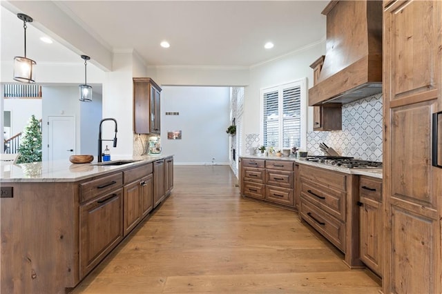 kitchen with a center island, stainless steel gas cooktop, decorative light fixtures, custom range hood, and light wood-type flooring