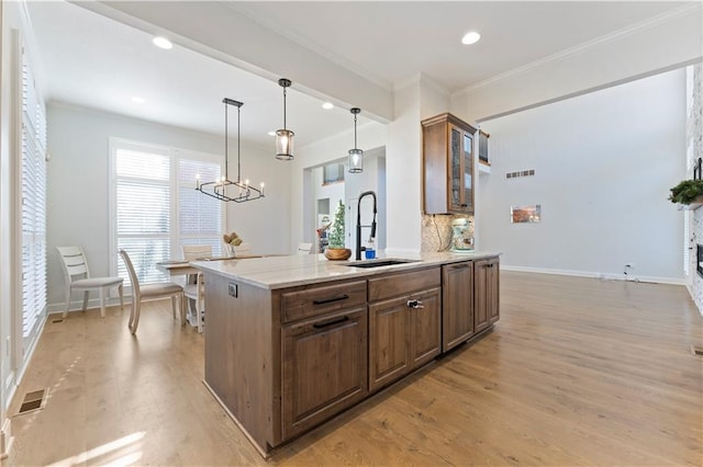 kitchen with light stone countertops, sink, hanging light fixtures, crown molding, and light hardwood / wood-style floors