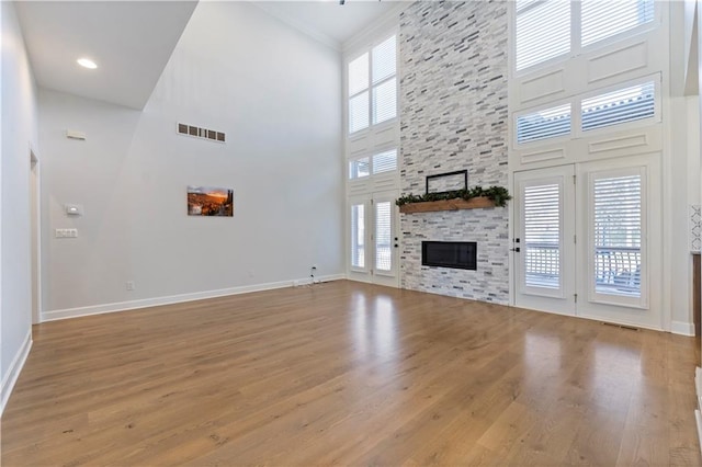 unfurnished living room featuring light hardwood / wood-style floors, crown molding, a towering ceiling, and a fireplace