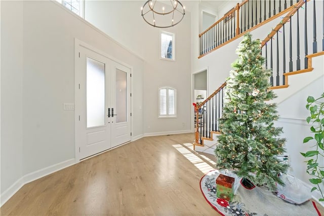 foyer featuring an inviting chandelier, wood-type flooring, a towering ceiling, and french doors