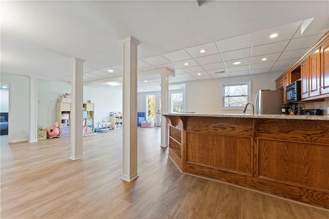 kitchen featuring a paneled ceiling, stainless steel fridge, light wood-type flooring, ornate columns, and kitchen peninsula