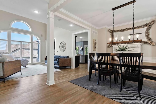 dining area featuring hardwood / wood-style flooring, a notable chandelier, crown molding, and decorative columns