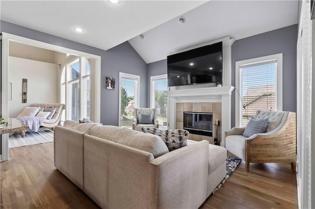 living room featuring hardwood / wood-style floors, lofted ceiling, and a tiled fireplace